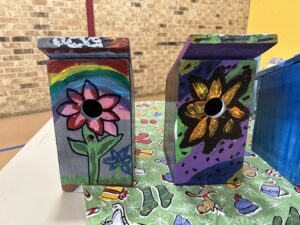 Two TNC student painted birdhouses featuring vibrant flowers