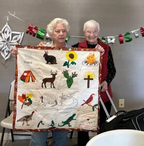 Two members of the Giver Connection of Kerr County hold a quilt that was made by the boys at Pathways.